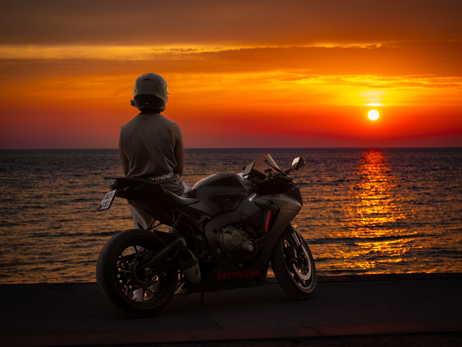 A rider seated on a motorcycle at sunset by the water